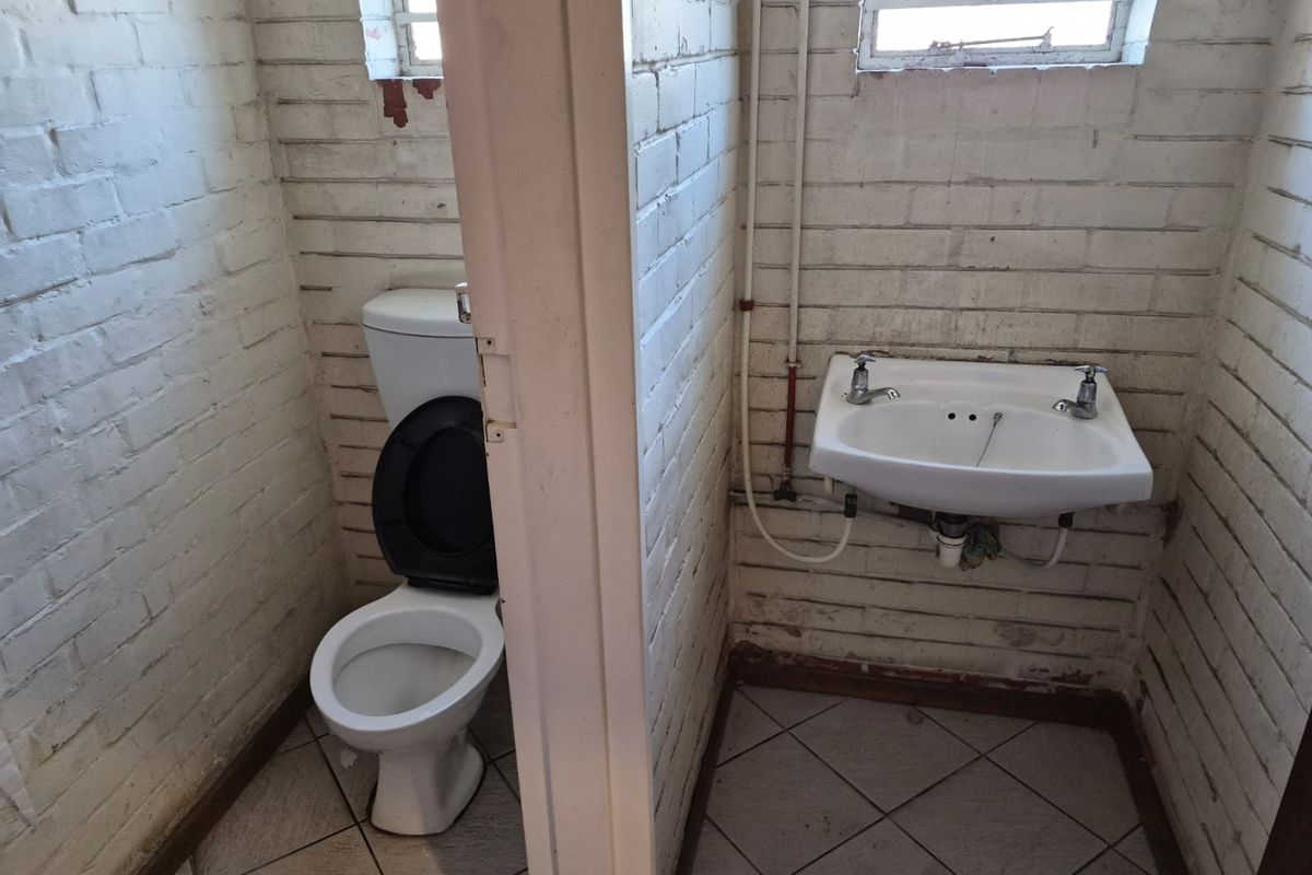 A basic industrial-style bathroom featuring a toilet and wall-mounted basin with exposed plumbing and painted brick walls.