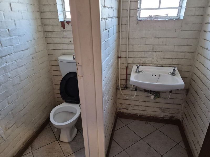 A basic industrial-style bathroom featuring a toilet and wall-mounted basin with exposed plumbing and painted brick walls.