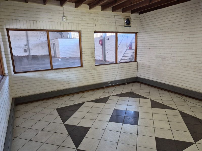Empty office space featuring exposed timber ceiling beams, painted brick walls, and patterned tiled flooring with integrated electrical trunking.