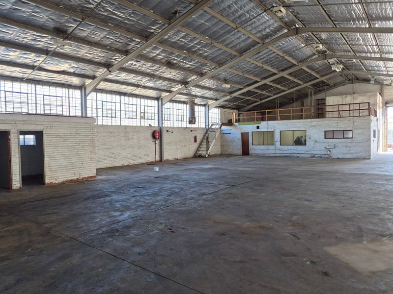 Spacious industrial warehouse featuring high ceilings with exposed steel trusses, concrete flooring, mezzanine level, and ample natural light through large industrial windows.