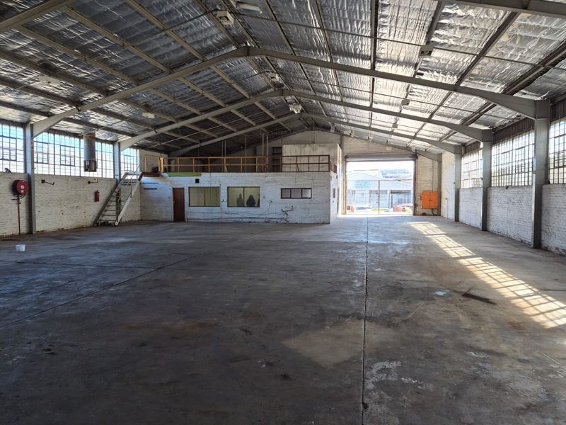 Spacious industrial warehouse featuring high ceilings with reflective insulation, concrete flooring, a mezzanine level, and a large roller shutter door for easy access.