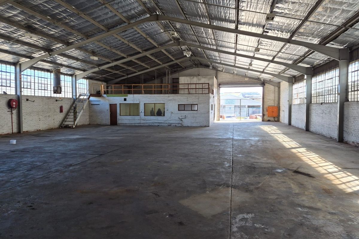Spacious industrial warehouse featuring high ceilings with reflective insulation, concrete flooring, a mezzanine level, and a large roller shutter door for easy access.