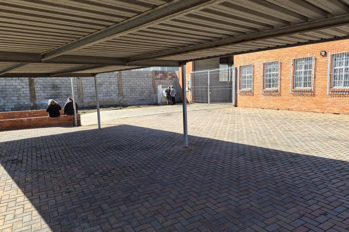 Industrial property exterior featuring a covered carport area, brick paving, and a secure fenced yard with face brick building facade.