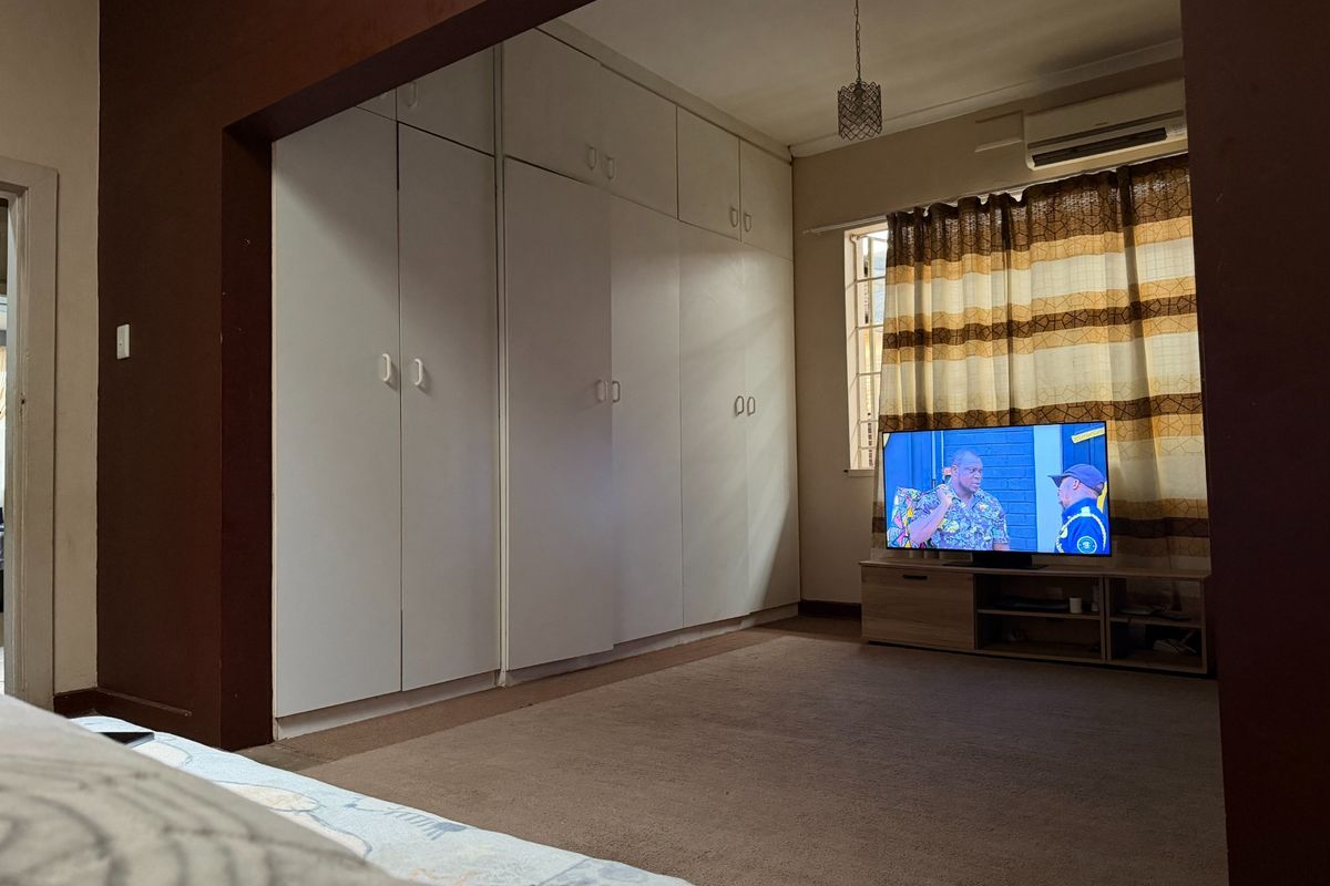 A bedroom featuring extensive built-in cupboards, carpeted flooring, and a wall-mounted air conditioning unit.