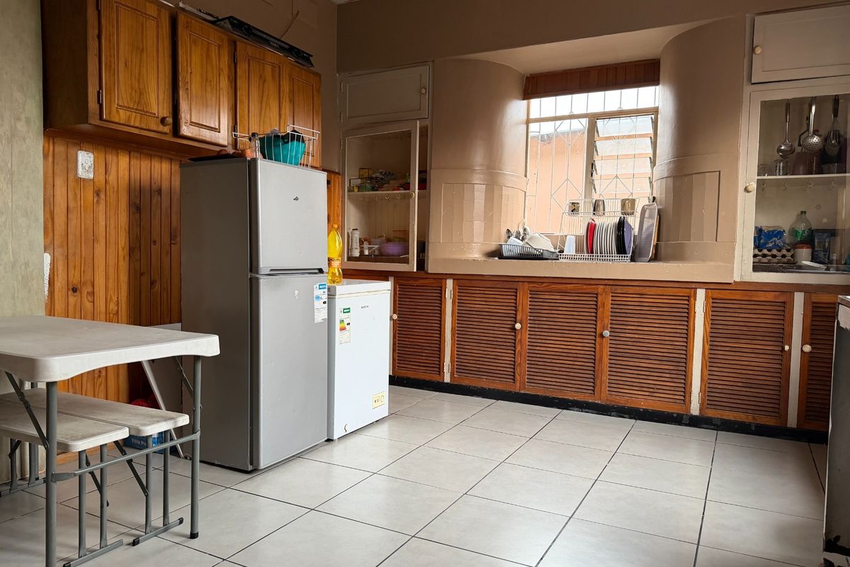A dated kitchen featuring wooden cabinetry, tiled flooring, and a window with security bars, offering potential for a modern renovation.