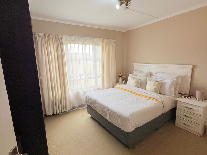 A well-lit bedroom featuring neutral wall tones, carpeted flooring, and a large window with security bars.
