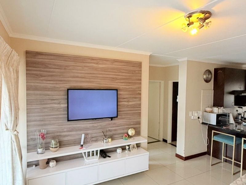 Open-plan living area featuring tiled floors, a modern built-in media wall, and an adjacent kitchen with a breakfast counter.