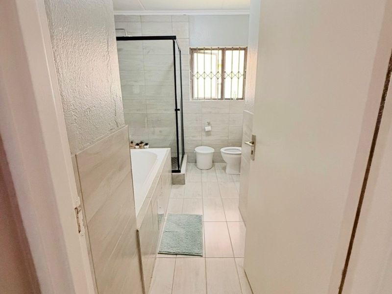 A clean, modern bathroom featuring a bathtub, separate shower enclosure with black frame, and a toilet, finished with neutral wall and floor tiles.