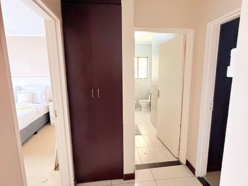 A clean, tiled hallway featuring a built-in dark wood cupboard, providing access to a bedroom and a bathroom.