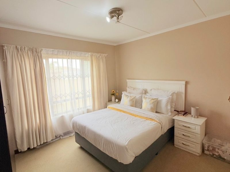 A well-lit bedroom featuring neutral wall tones, carpeted flooring, and a window fitted with a security gate.