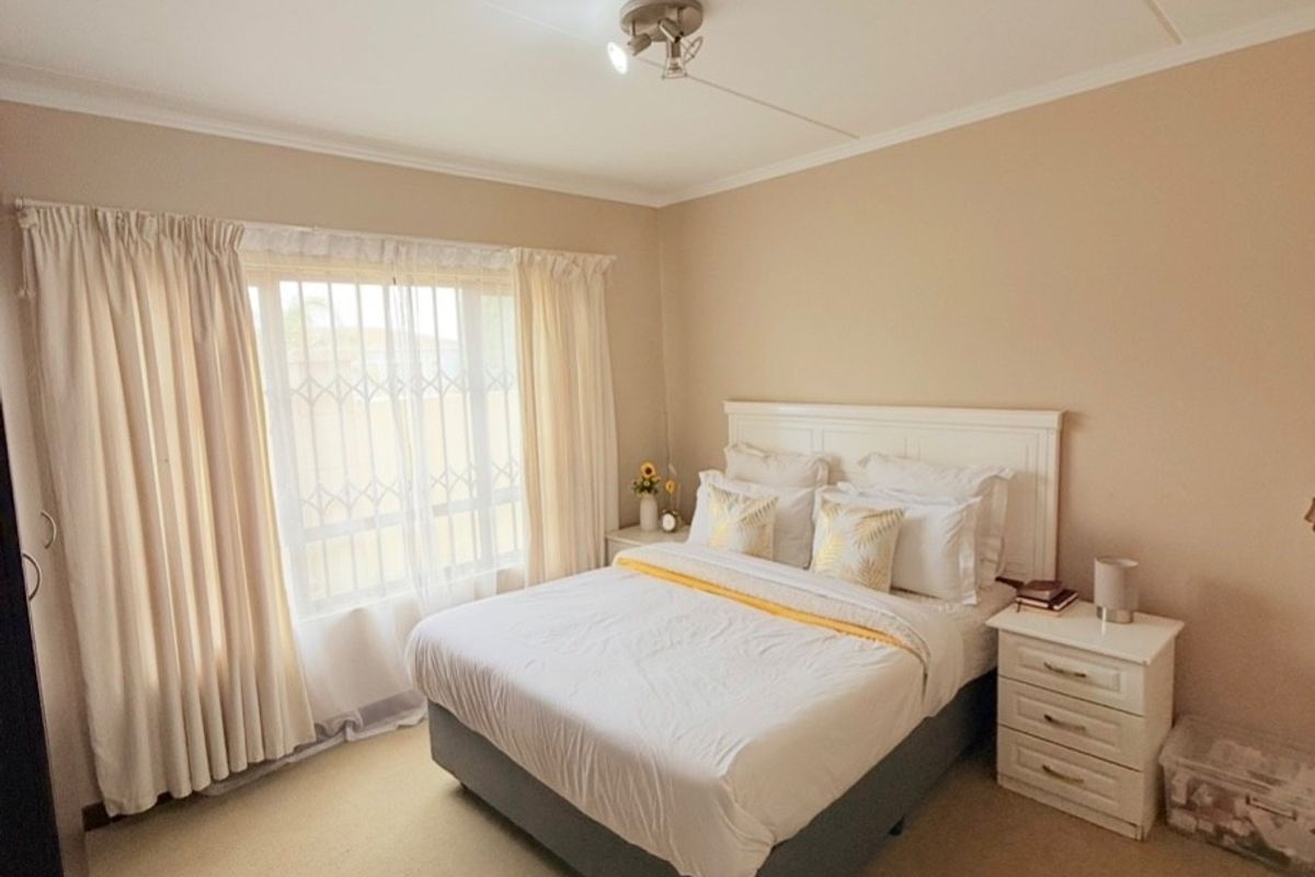A well-lit bedroom featuring neutral wall tones, carpeted flooring, and a window fitted with a security gate.