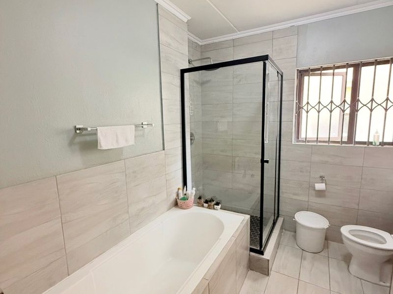 A well-maintained bathroom featuring a built-in bathtub, a separate glass-enclosed shower, and neutral floor-to-ceiling tiling.