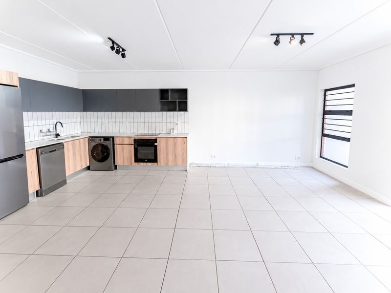 Modern open-plan kitchen and living area featuring neutral tiled flooring, contemporary two-tone cabinetry, built-in appliances, and ample natural light.