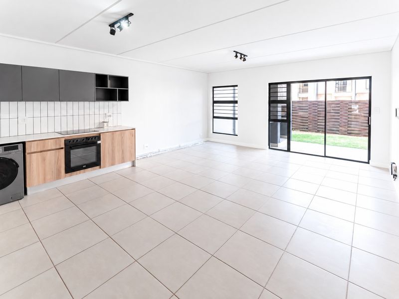 Spacious open-plan living and kitchen area featuring modern cabinetry, built-in oven and hob, tiled flooring, and large sliding doors leading to the garden.