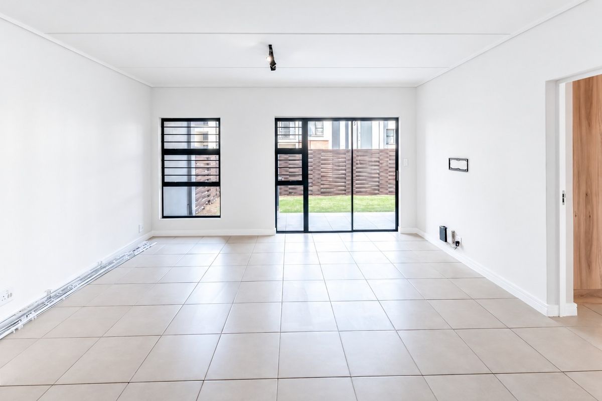 A bright, open-plan living area featuring neutral tiled flooring, modern aluminium window frames, and a sliding glass door leading to the outdoor space.