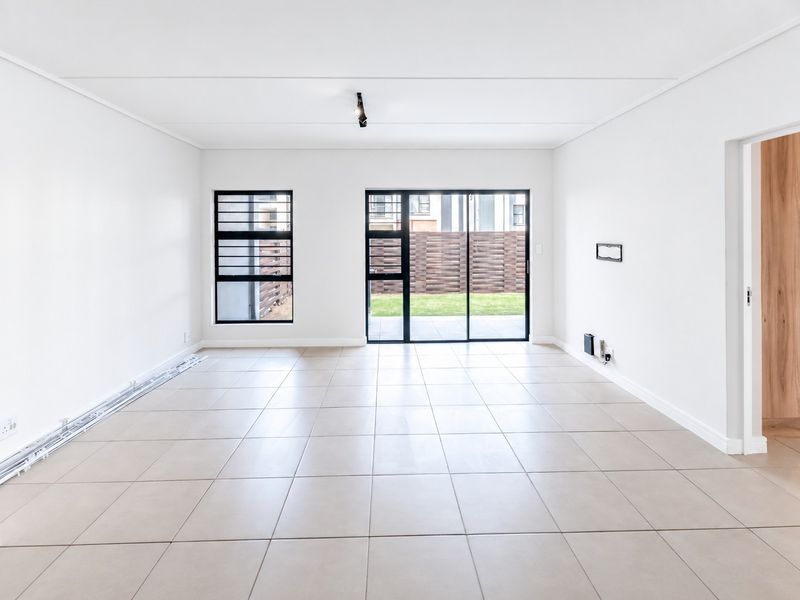 A bright, open-plan living area featuring neutral tiled flooring, modern aluminium window frames, and a sliding glass door leading to the outdoor space.