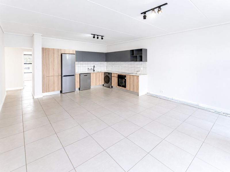 Modern open-plan kitchen featuring sleek wood-tone and grey cabinetry, tiled flooring, and integrated appliances in a bright, spacious living area.