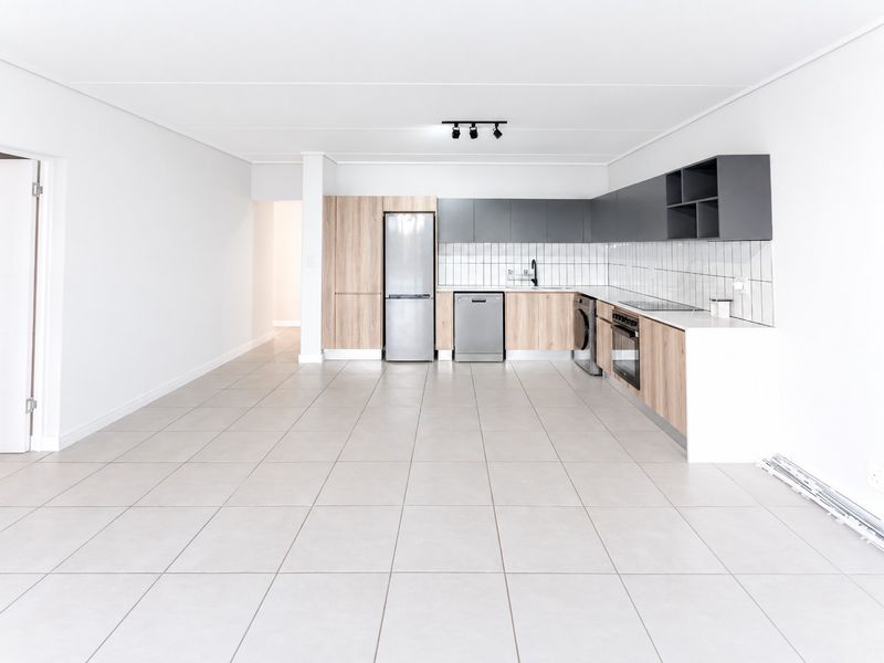 Modern open-plan kitchen featuring light wood and grey cabinetry, tiled flooring, and integrated appliances in a bright, spacious living area.