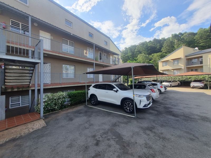 Exterior view of an apartment complex featuring a paved parking area with carports, metal staircases, and balcony access.