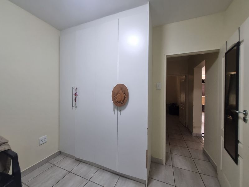 A bedroom featuring neutral walls, tiled flooring, and a white built-in wardrobe with modern handles.