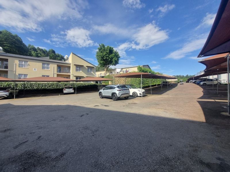 Exterior view of an apartment complex parking area featuring covered shade cloth carports and paved driveway access.