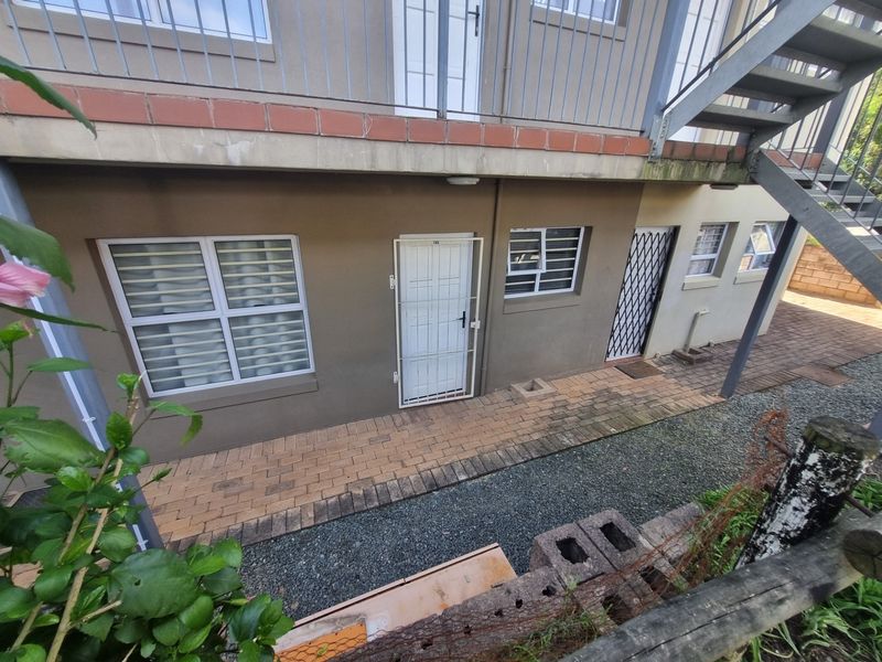 Rear exterior view of the apartment building featuring a paved walkway, security gates, and an external metal staircase leading to the upper level.