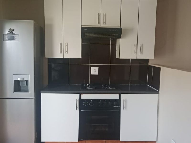 Compact kitchen featuring white cabinetry, dark tiled backsplash, built-in oven, gas hob, and extractor fan.