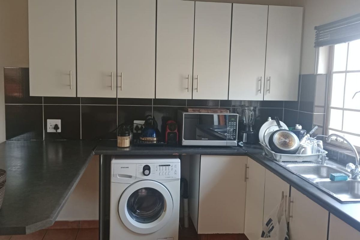 Functional kitchen featuring white cabinetry, dark laminate countertops, tiled splashbacks, and a dedicated space for a washing machine under the counter.