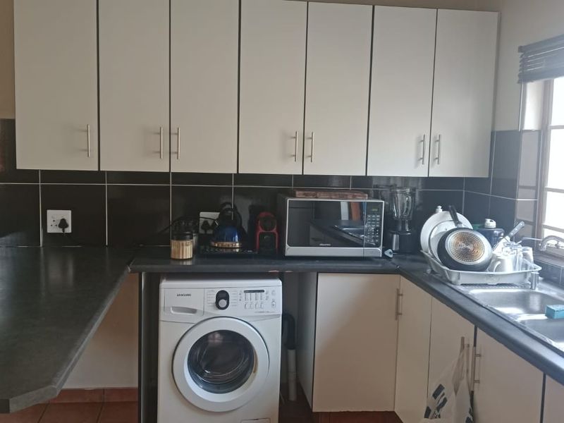 Functional kitchen featuring white cabinetry, dark laminate countertops, tiled splashbacks, and a dedicated space for a washing machine under the counter.