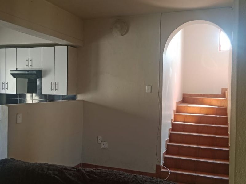 Open plan living area featuring a compact kitchen with white cabinetry and an arched staircase leading to the upper level.