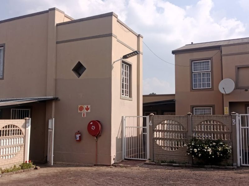 Front view of a multi-unit residential complex featuring paved driveway access, security gates, and exterior fire safety equipment.