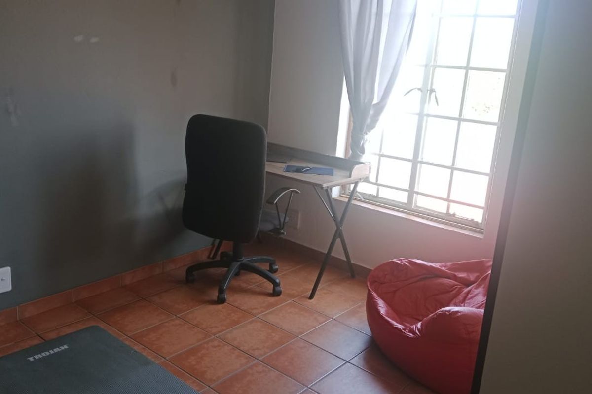 A bedroom featuring tiled flooring and a window with security bars, currently utilized as a home office space.