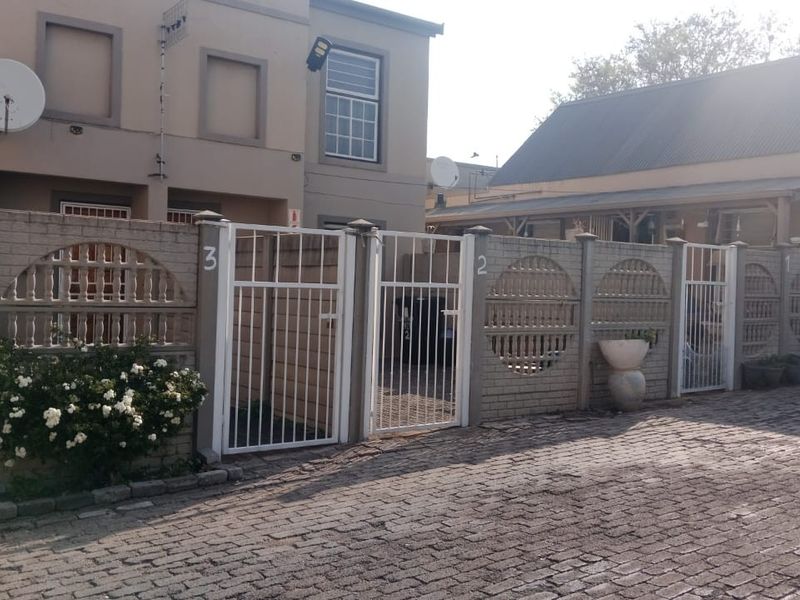 Street view of a residential complex featuring a cobblestone driveway, precast concrete boundary walls, and secure metal entrance gates.