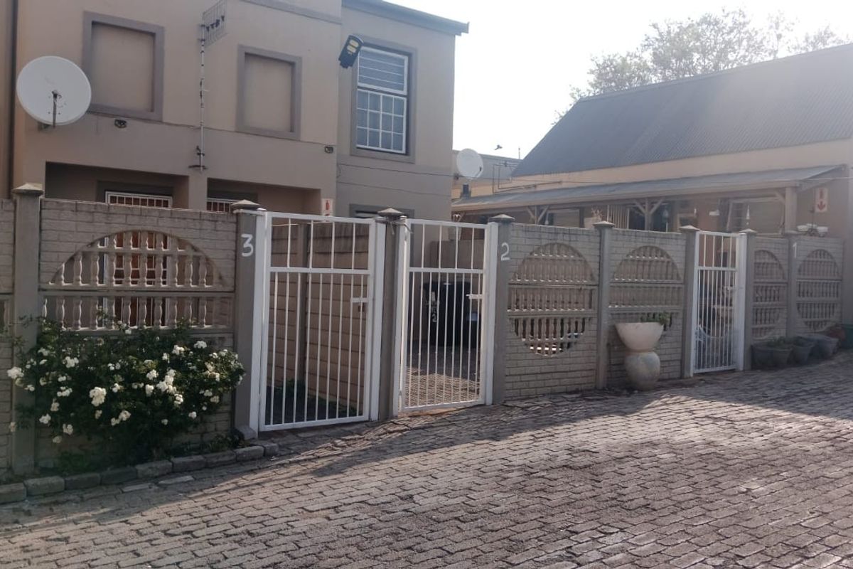 Street view of a residential complex featuring a cobblestone driveway, precast concrete boundary walls, and secure metal entrance gates.