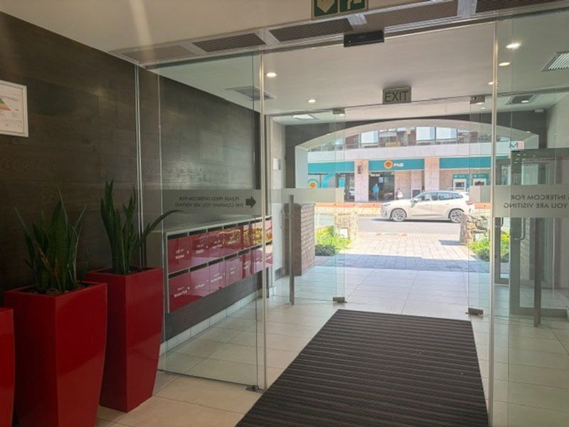 Modern office building entrance lobby featuring glass doors, built-in mailboxes, and tiled flooring with direct access to the street.
