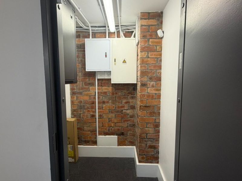 A functional utility space featuring exposed brickwork, surface-mounted electrical distribution boards, and conduit, providing essential infrastructure access.