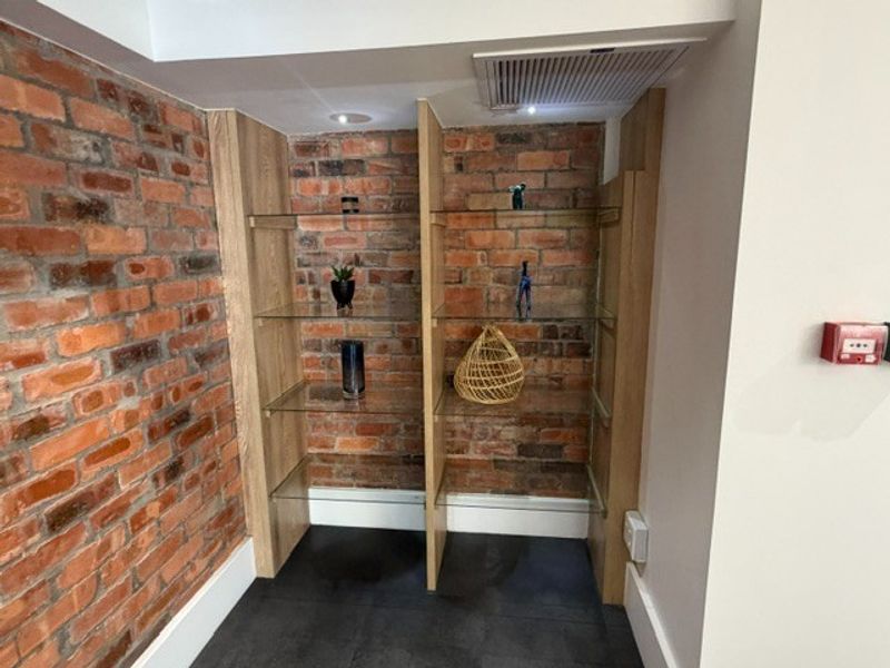 A modern office alcove featuring exposed brick walls, built-in timber-framed glass shelving, recessed lighting, and sleek dark tiled flooring.