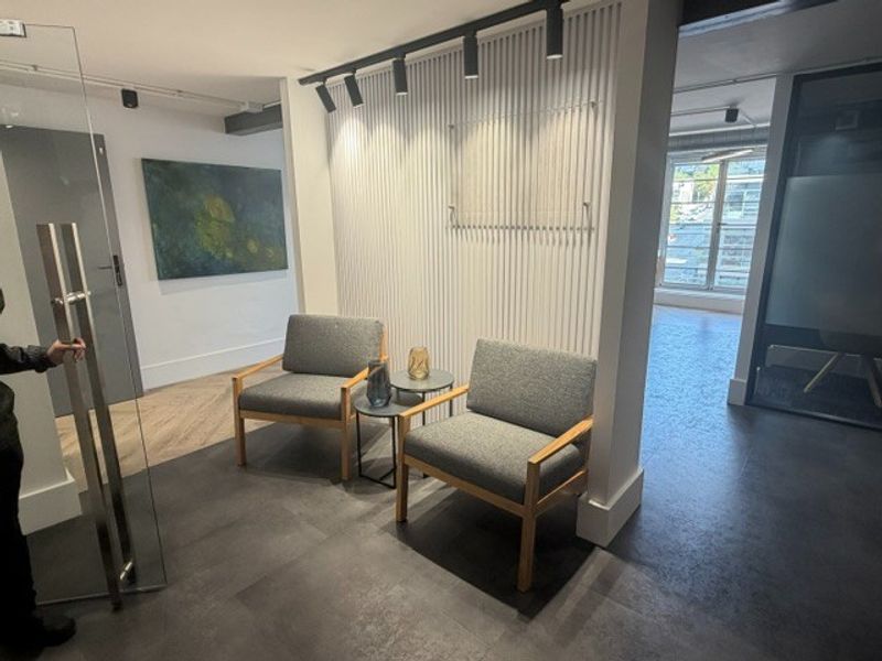 Modern office reception area featuring contemporary slatted wall paneling, track lighting, and a mix of tiled and laminate flooring with a glass entrance door.