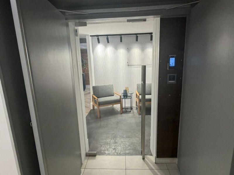 Modern office entrance featuring a glass door, integrated access control system, contemporary slatted wall paneling, and professional track lighting.