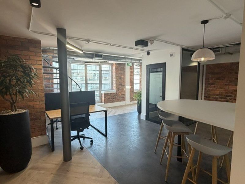 Modern industrial-style office space featuring exposed brick walls, herringbone flooring, exposed ceiling ducting, and a spiral staircase, creating a contemporary professional work environment.