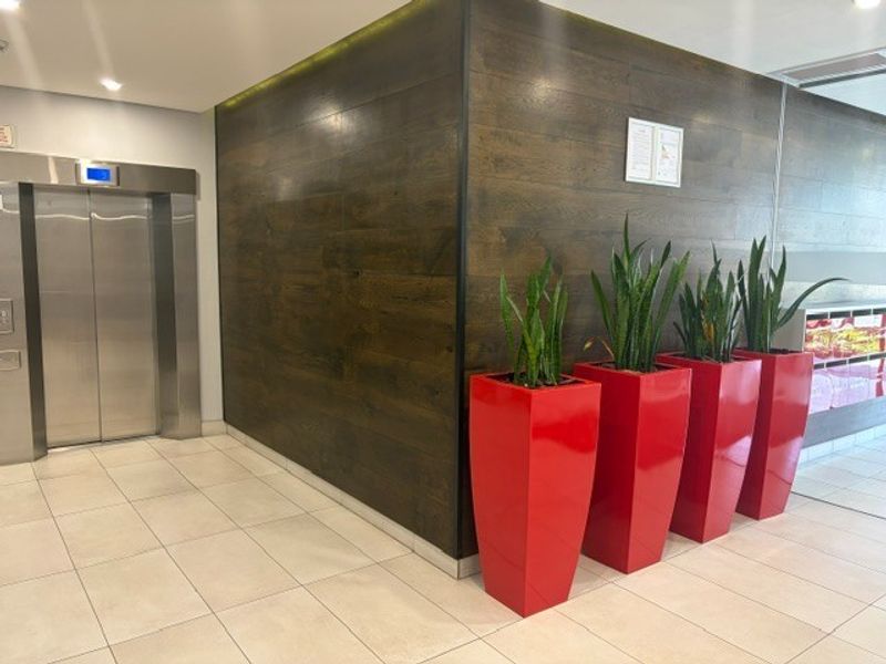 Modern office building lobby entrance featuring a stainless steel elevator, tiled flooring, and decorative wood-look wall paneling.