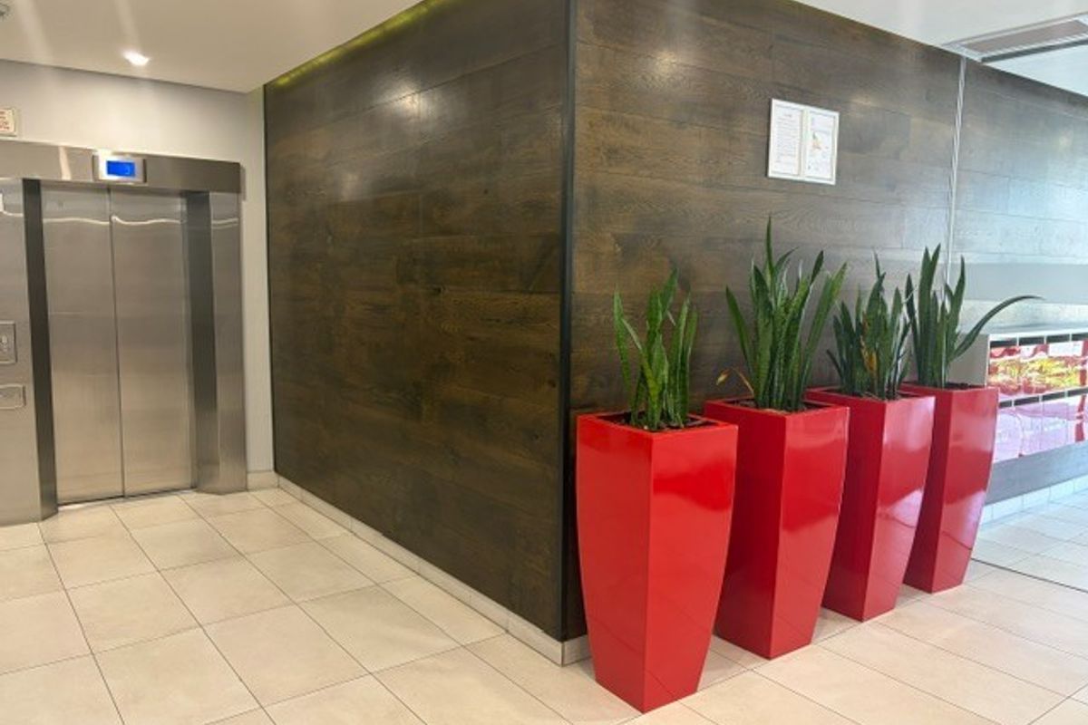 Modern office building lobby entrance featuring a stainless steel elevator, tiled flooring, and decorative wood-look wall paneling.