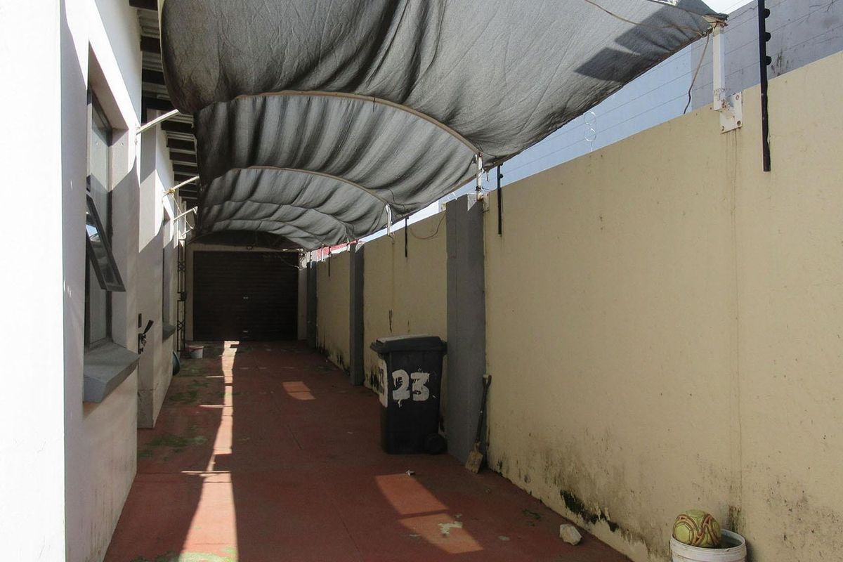 A narrow exterior side passage featuring a shade cloth canopy, perimeter wall with electric fencing, and direct access to a garage.