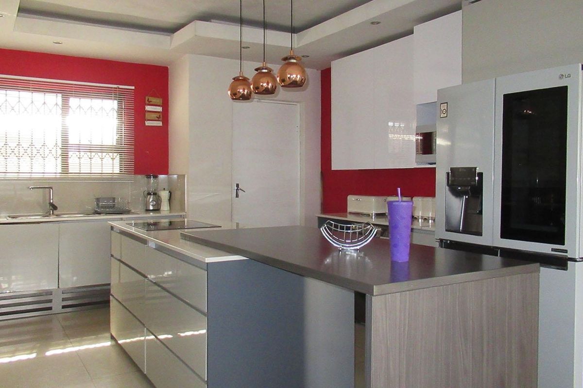 Modern kitchen featuring a central island, sleek cabinetry, contrasting red accent walls, and contemporary pendant lighting.