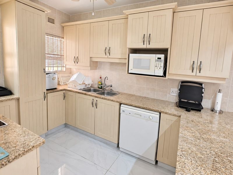 A functional kitchen featuring cream-colored cabinetry, granite countertops, a double bowl sink, and tiled finishes, offering a clean and practical workspace.