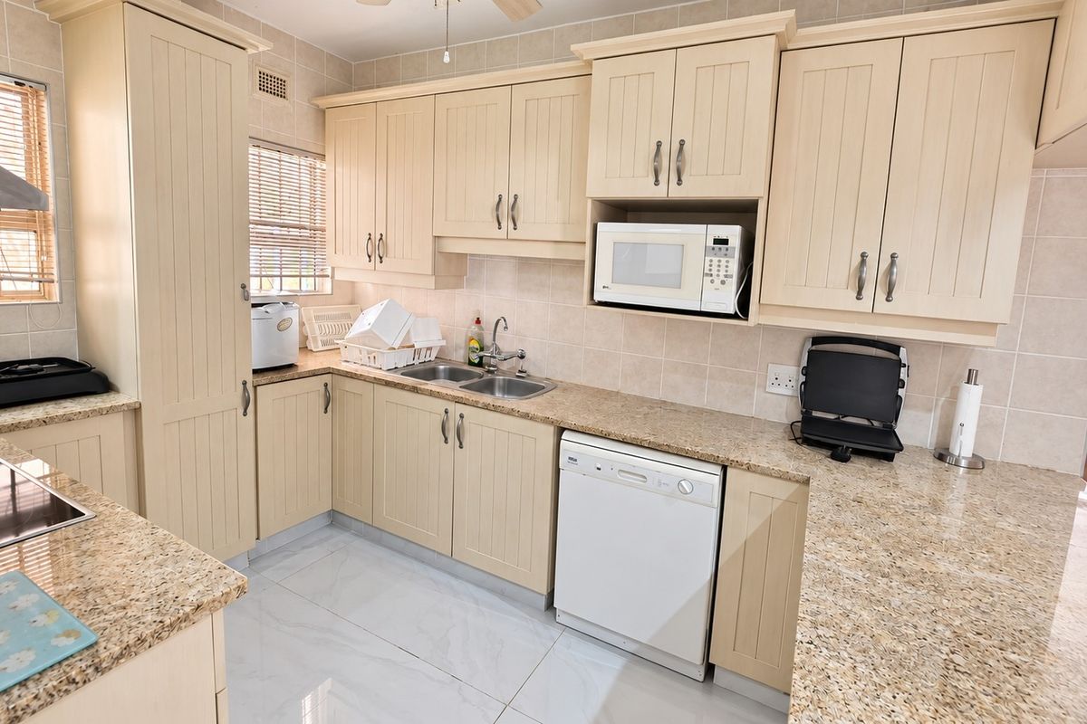 A functional kitchen featuring cream-colored cabinetry, granite countertops, a double bowl sink, and tiled finishes, offering a clean and practical workspace.