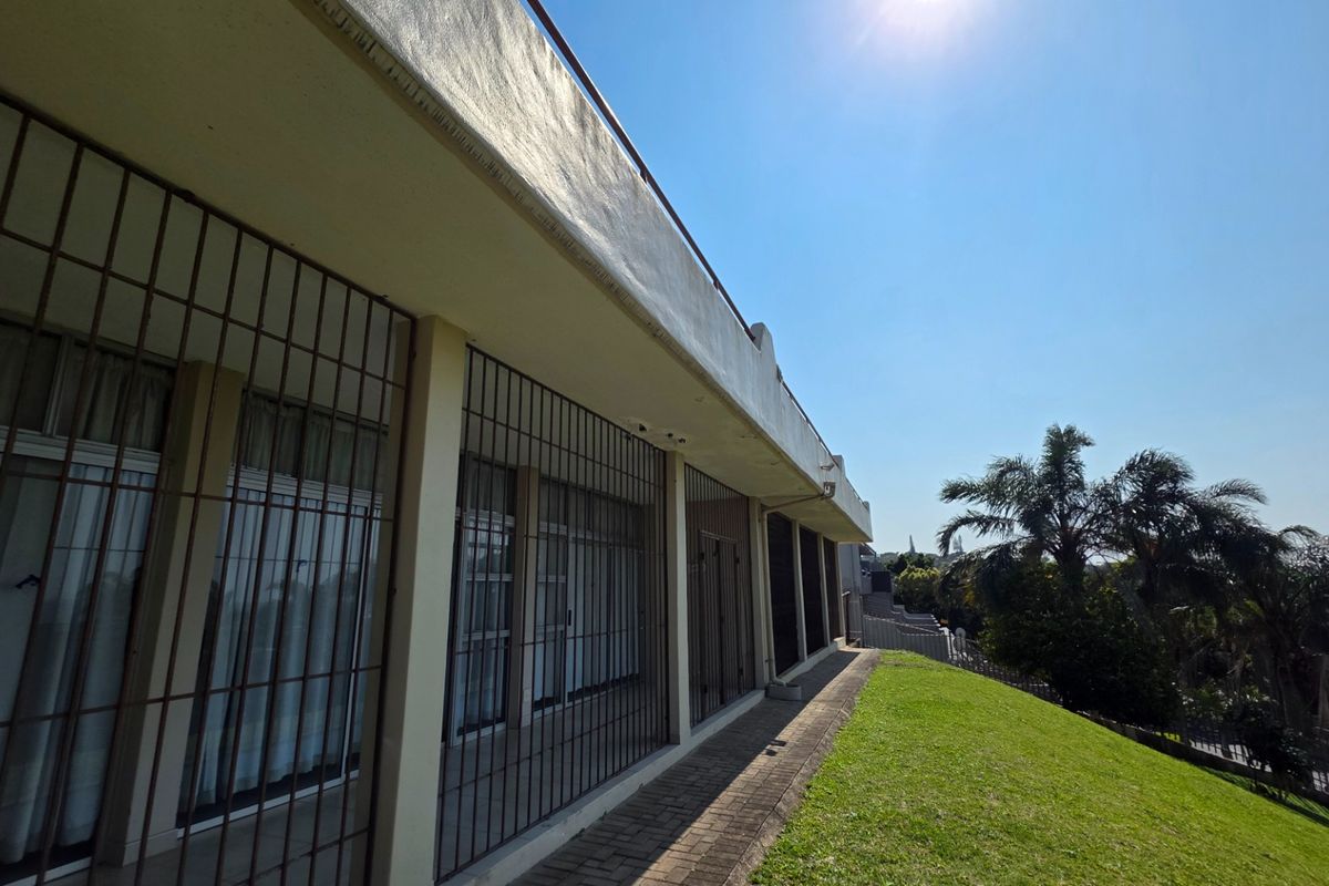 Rear exterior view of the apartment featuring a paved walkway, lawn area, and security bars installed on the windows.