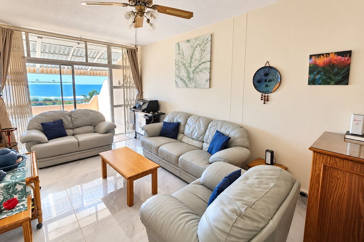A bright living room featuring tiled floors, a ceiling fan, and large sliding glass doors that open to a balcony with ocean views.