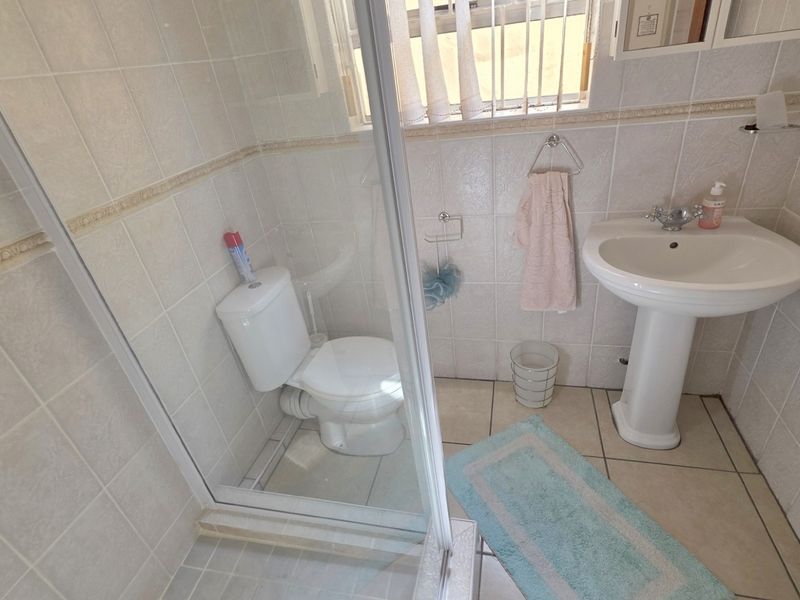 A functional bathroom featuring a pedestal basin, toilet, and a glass-enclosed shower, finished with neutral ceramic wall and floor tiles.