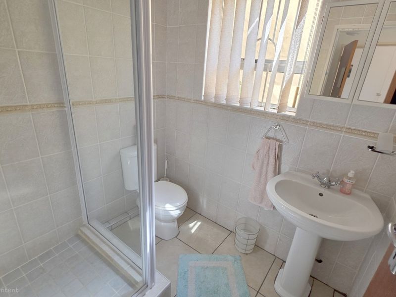 A functional bathroom featuring a pedestal basin, a glass-enclosed shower, and tiled finishes throughout.